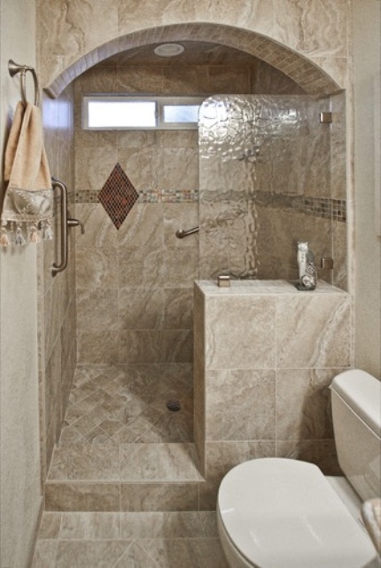 un bagno in piastrelle di pietra neutra con uno spazio doccia ad arco e una piccola finestra per una luce più naturale