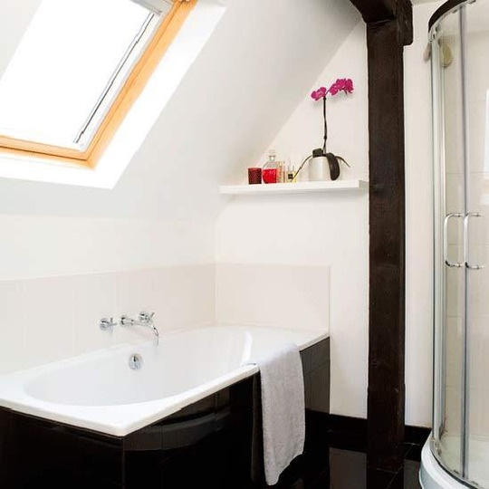 un elegante bagno a contrasto con piastrelle bianche e una vasca rivestita con piastrelle nere più un lucernario per una luce più naturale