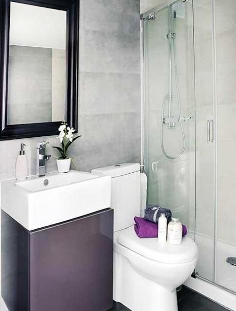 un piccolo bagno minimalista con pareti di cemento, uno spazio doccia, un lavabo viola e uno specchio in una cornice scura