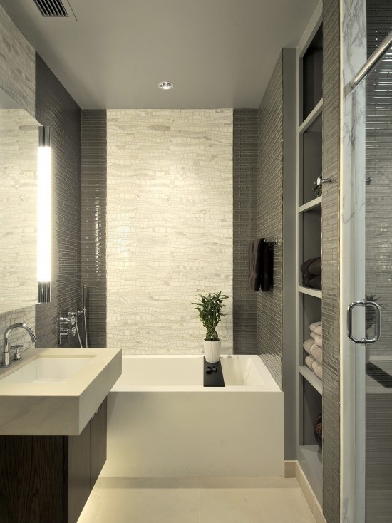 un bagno grigio e bianco fatto con piastrelle piccole e accattivanti, un lavandino e una vasca quadrati e uno spazio di archiviazione incorporato