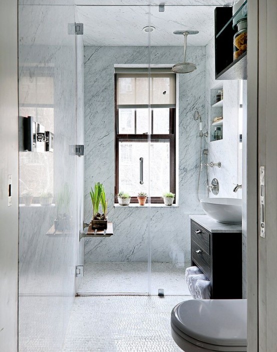 un piccolo bagno con piastrelle in pietra blu sotto la doccia, un lavabo macchiato di scuro, piante in vaso e mensole incorporate