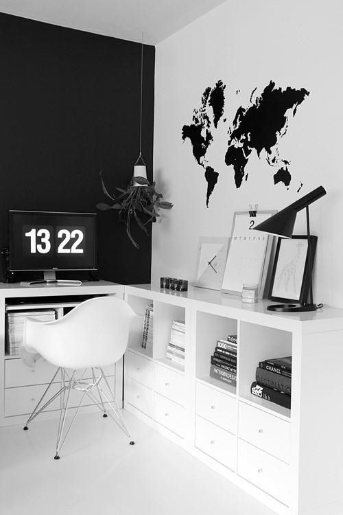 un ufficio domestico minimalista in bianco e nero con un muro nero, una mappa sul muro, un comodo contenitore e una sedia bianca