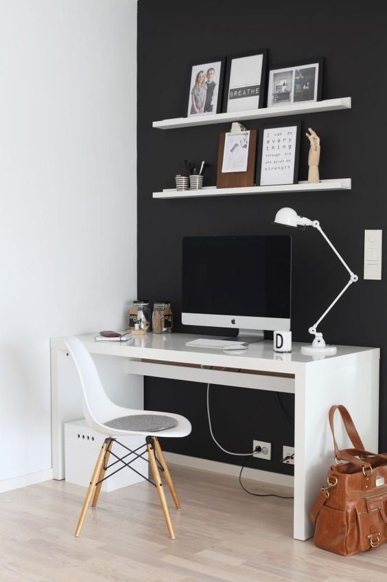 un ufficio domestico minimalista in bianco e nero con un muro nero, mobili bianchi e alcune opere d'arte