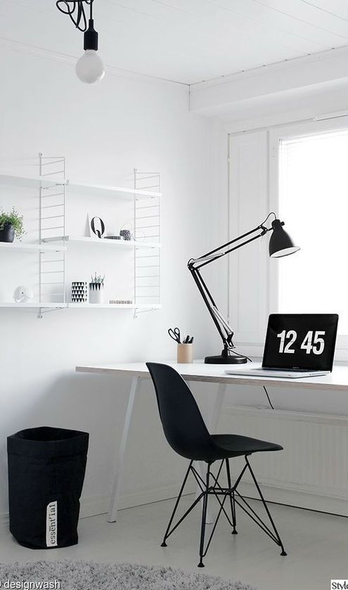 un semplice home office nordico in bianco e nero con una scrivania bianca, uno scaffale, una sedia nera e un cesto portaoggetti in tessuto
