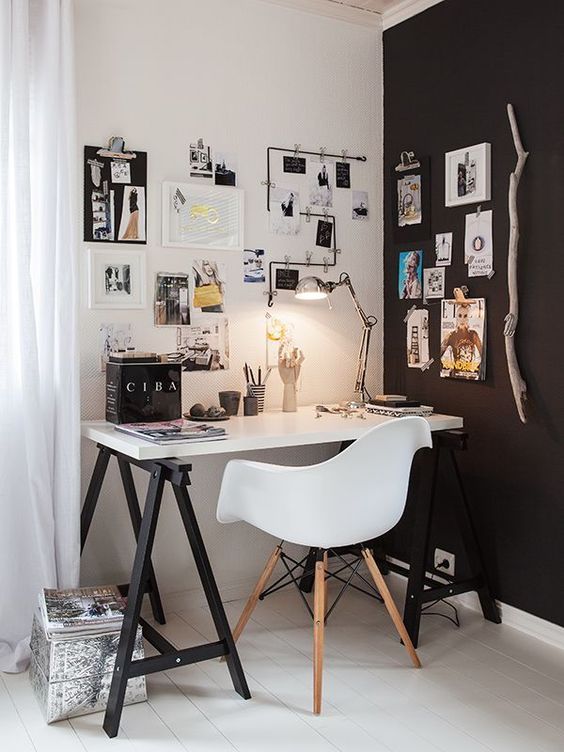 un elegante ufficio in casa scandinavo con un muro bianco e nero, una scrivania in bianco e nero a cavalletto e alcune opere d'arte in bianco e nero