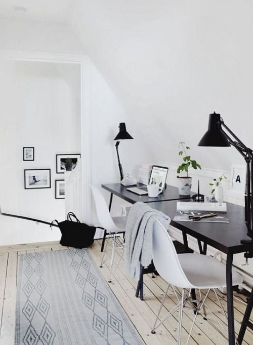 un accogliente spazio scandinavo con una scrivania nera e sedie bianche, lampade nere e tappeti stampati