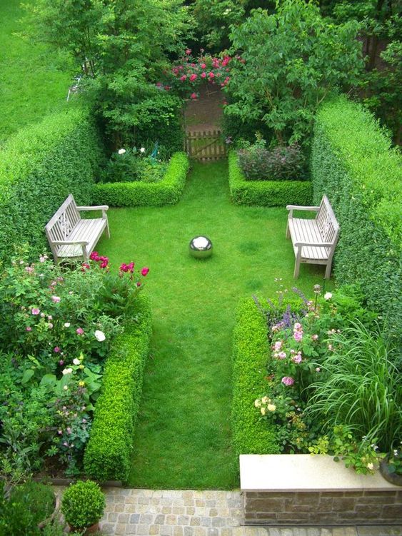 un lussureggiante giardino di una casa a schiera con molta vegetazione, pareti viventi che incorniciano le aiuole, panchine di legno e alcune pietre