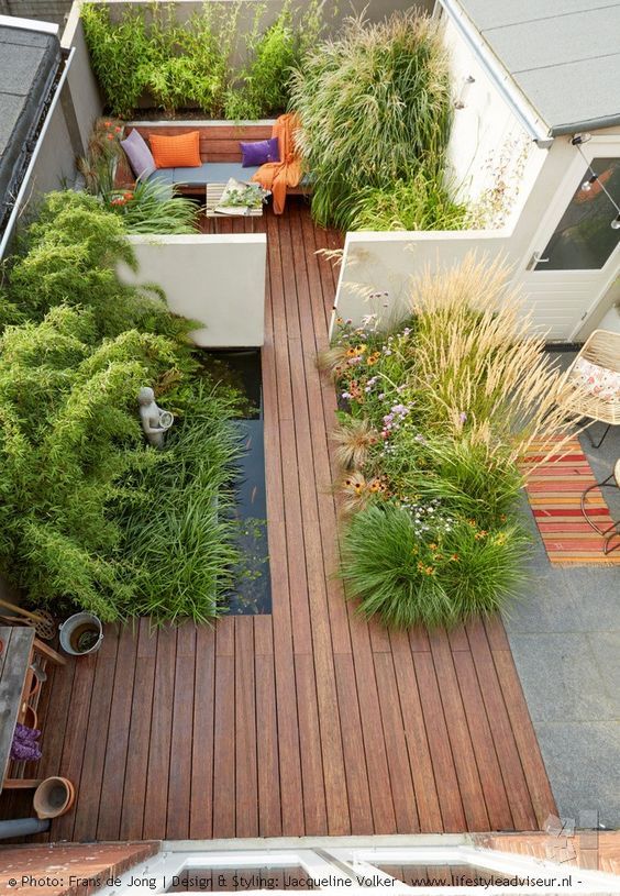 un giardino minimalista in una casa a schiera con un ponte di legno, uno stagno, erbe ed erbe piantate e una panchina incorporata