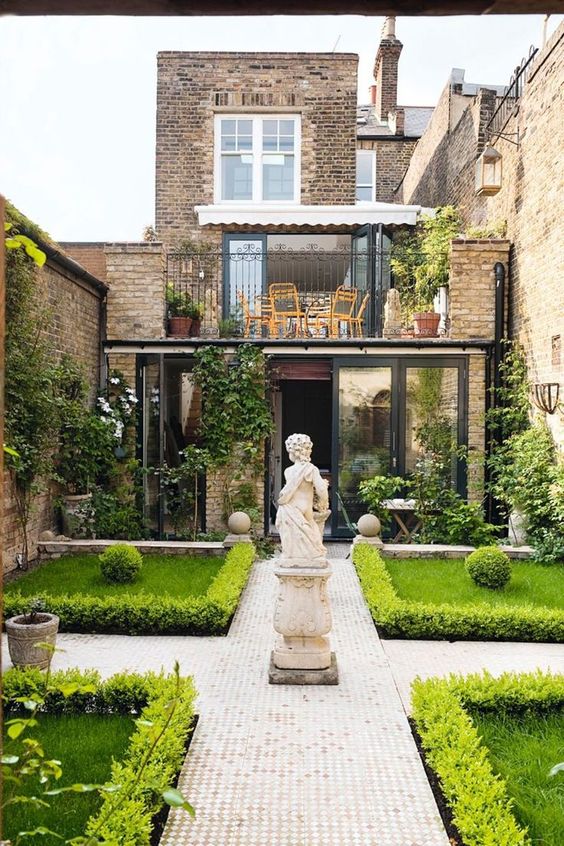 un insolito giardino a schiera ispirato ai classici, con prati ben curati allineati con vegetazione, piastrelle a mosaico e una grande statua al centro