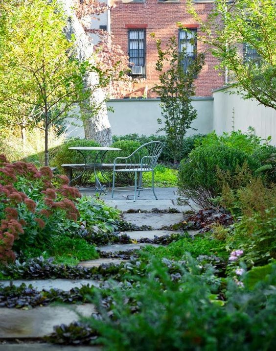 un giardino di una casa a schiera con alberi e vegetazione lussureggiante che cresce anche tra i gradini di pietra e i mobili di metallo