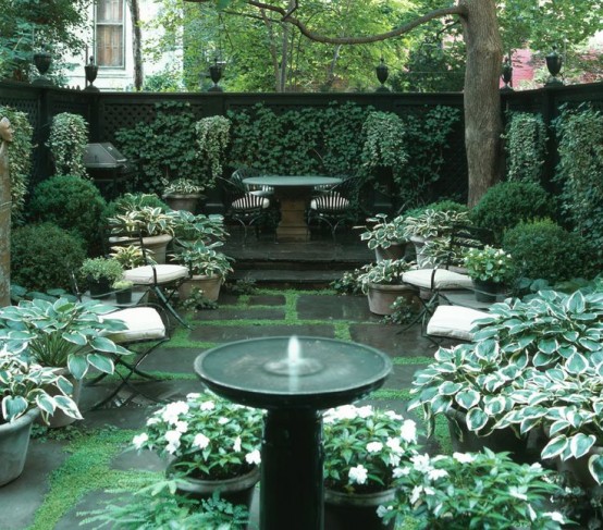 un accogliente giardino ombreggiato con pareti viventi e piante in vaso più alcuni mobili da giardino e una piccola fontana