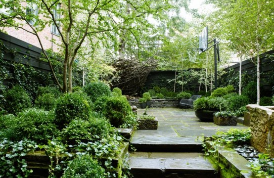 un giardino lussureggiante con terrazza e gradini in pietra, pareti viventi e vegetazione in vaso più un anello di pallacanestro