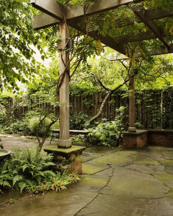 un giardino di una casa a schiera con una staccionata in legno, vegetazione piantumata e una capanna di legno, il tutto ricoperto di vegetazione vivente