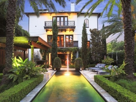 un grande giardino in una casa a schiera con una piscina con cascata, alberi piantati, palme e vegetazione, oltre a mobili contemporanei