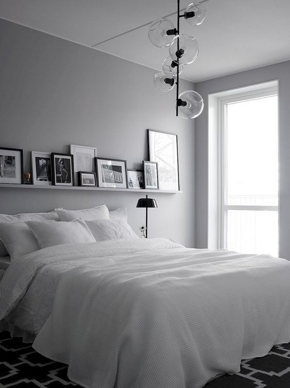 una camera da letto nordica monocromatica con lampade a sospensione, un letto bianco, una sporgenza con opere d'arte e lampade nere