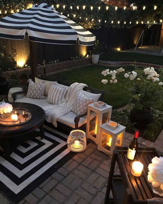 un accogliente patio con un tappeto a righe, lanterne a candela e fiori in vaso che rinfrescano l'aspetto
