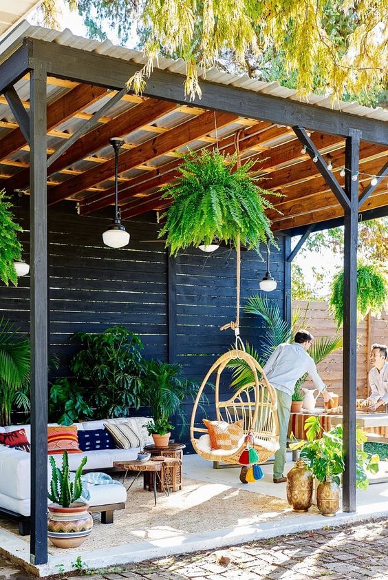 un patio luminoso con piante in vaso, cuscini colorati, una sedia sospesa in rattan e lampade a sospensione