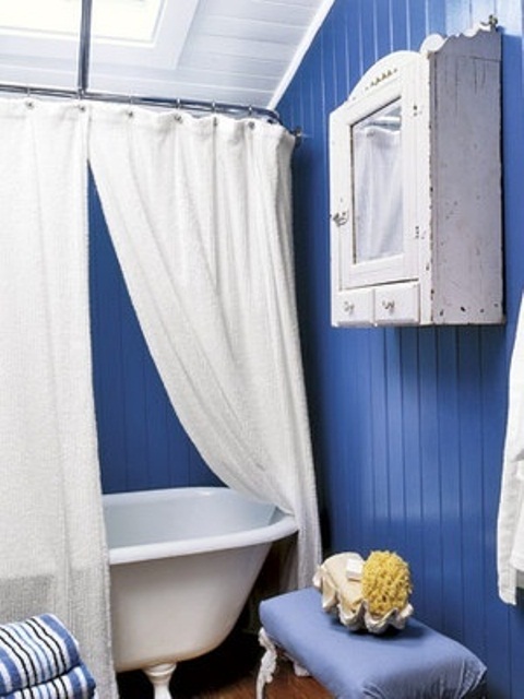 un audace bagno blu e bianco con una tenda neutra, un armadio shabby chic e uno sgabello vintage blu