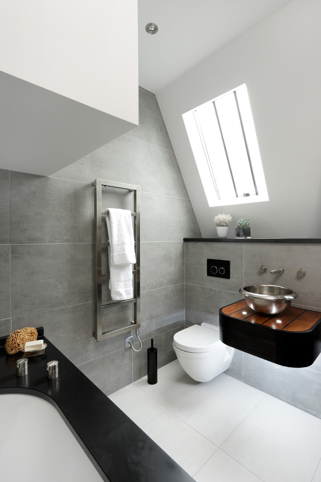un audace bagno in mansarda con piastrelle grigie, un piccolo lavabo nero, una vasca rivestita di nero e un pavimento bianco (CUBIC Studios Limited)