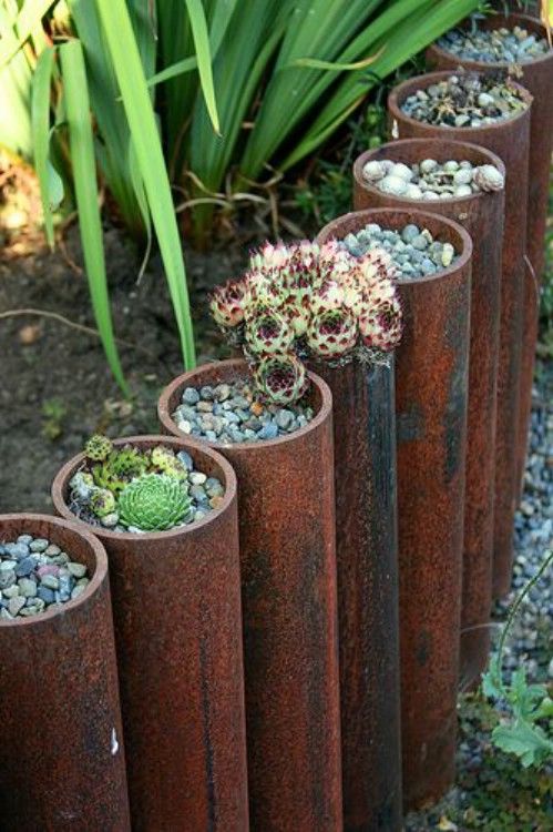 grandi tubi di metallo con piante grasse piantate con ciottoli sono un'idea unica e creativa per delimitare il tuo giardino