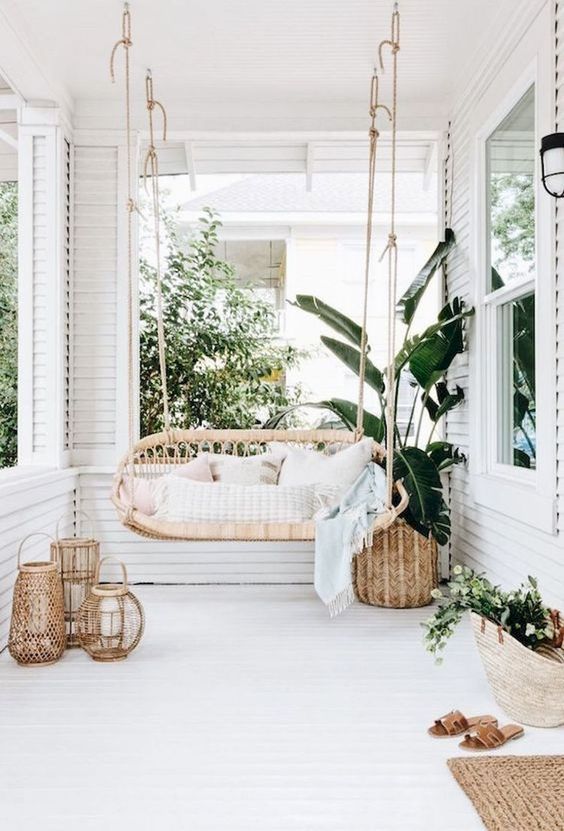 un accogliente patio tropicale con un divano letto sospeso in rattan, lanterne a candela in rattan, un tappeto di iuta e fioriere in vimini