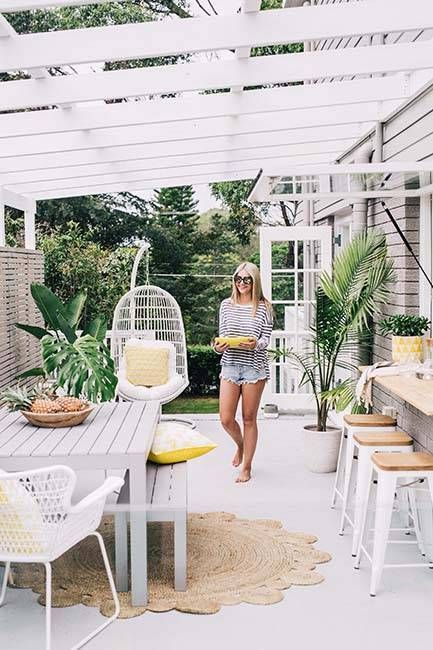 una terrazza tropicale con una finestra passante come bancone del bar e uno spazio per mangiare, piante in vaso e una sedia sospesa in rattan per un'atmosfera tropicale