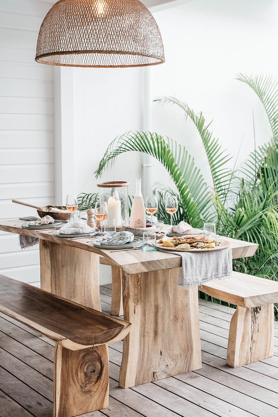 uno spazio da pranzo tropicale all'aperto con mobili in legno grezzo, un paralume in vimini e piante in vaso