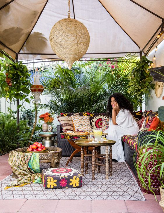 un luminoso patio tropicale boho con una tenda in cima, tessuti boho, cuscini colorati e molte piante in vaso intorno