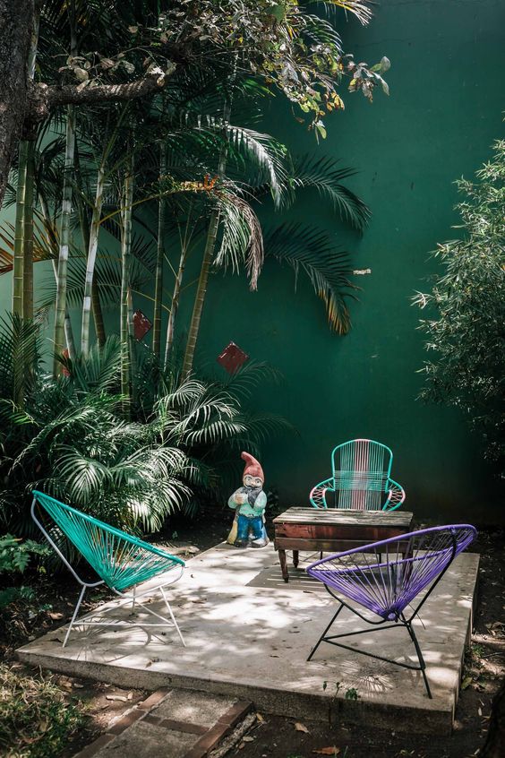 un semplice patio tropicale con sedie colorate, un tavolo in legno vintage e molte piante tropicali che crescono intorno