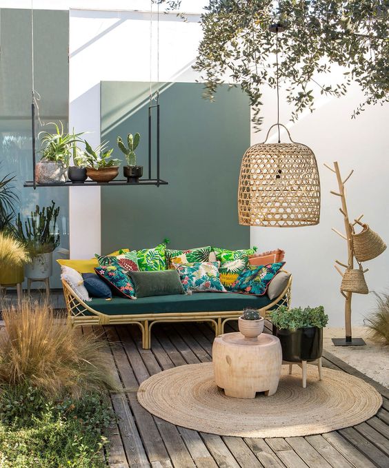 un'accogliente terrazza tropicale con un divano in rttan, cuscini colorati, un tappeto di iuta, cesti di vimini e un paralume di vimini più piante in vaso