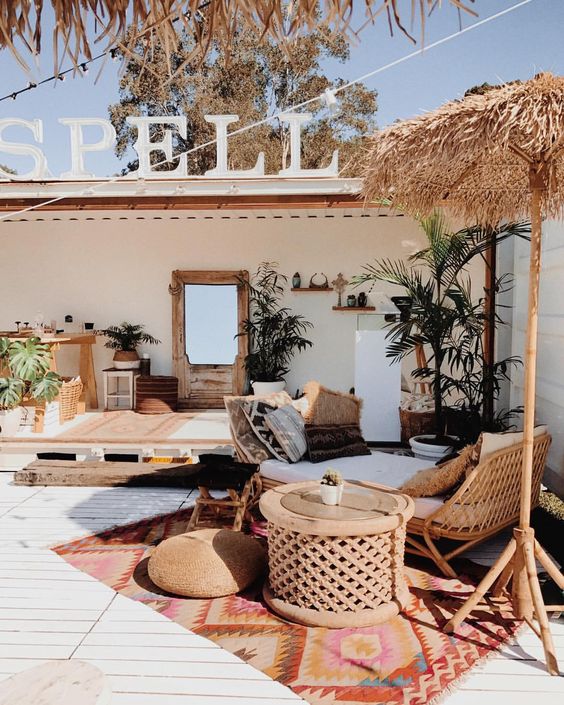 un patio tropicale con mobili in rattan, palme in vaso, cuscini, tappeti boho e un ombrellone sul divano
