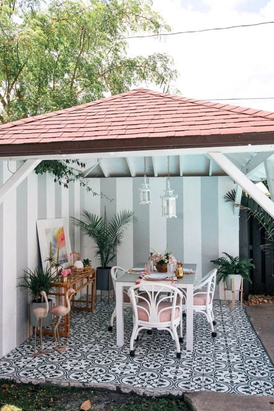 un patio tropicale con una sala da pranzo fatta con sedie in rattan bianche e rosa, fenicotteri rosa, un tavolo da bar in rattan e piante in vaso