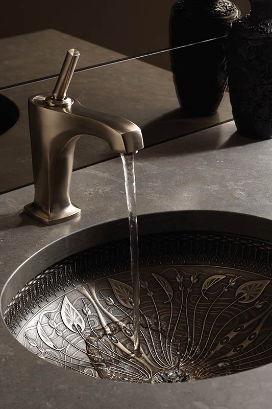 un lavabo in pietra con un lavandino in metallo decorato e un rubinetto opaco