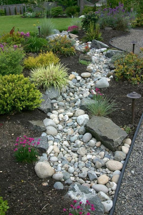 un giardino bello e di bassa manutenzione che incorpora un ruscello secco di roccia di fiume con erbe e fiori intorno