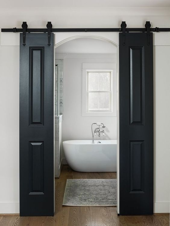 le porte scorrevoli nere del fienile contrastano lo spazio neutro e nascondono l'ingresso al bagno