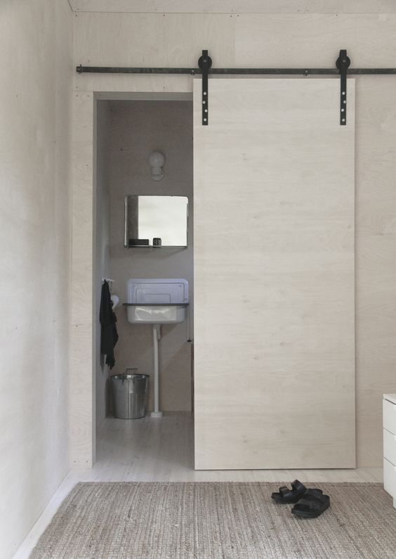 una porta scorrevole in compensato bianco nasconde il bagno e consente di risparmiare spazio