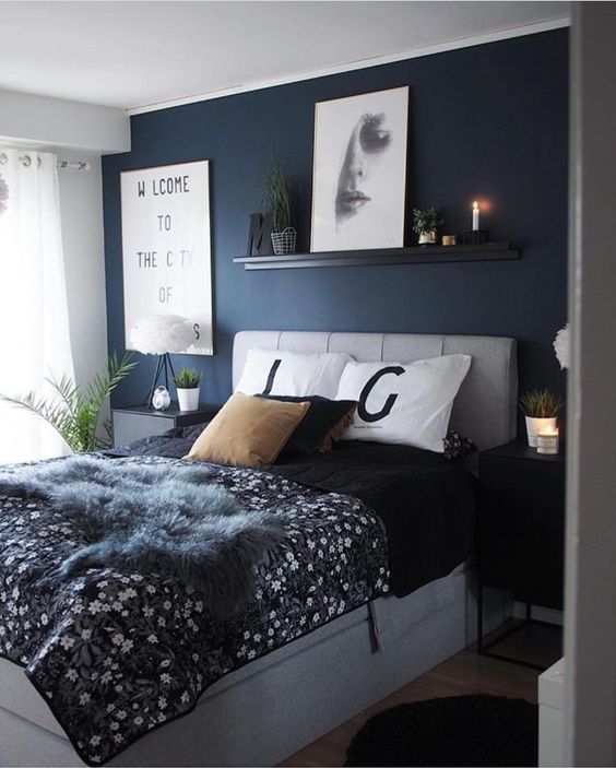 una camera da letto grigia e blu scuro con un muro di tendenza, un letto imbottito grigio e comodini, alcune opere d'arte moderne