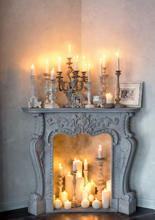 un raffinato camino vintage imbiancato a calce con candele di varie dimensioni e forme, con portacandele vintage