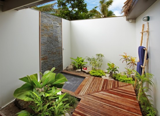 un accogliente angolo doccia esterno con pavimento in legno, muro rivestito in pietra e tanto verde piantato qui