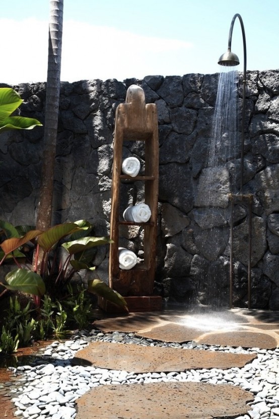 una doccia esterna grezza con muri in pietra, pavimenti in ciottoli, vegetazione piantumata e una mensola per asciugamani