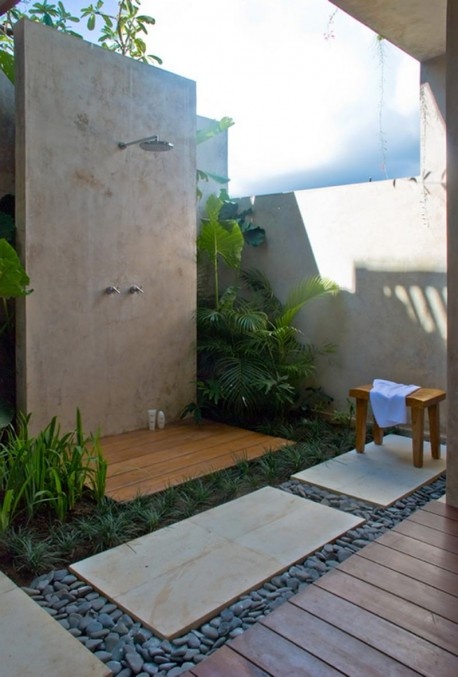 un'accogliente doccia esterna con piastrelle in pietra, ciottoli, vegetazione tropicale e accessori