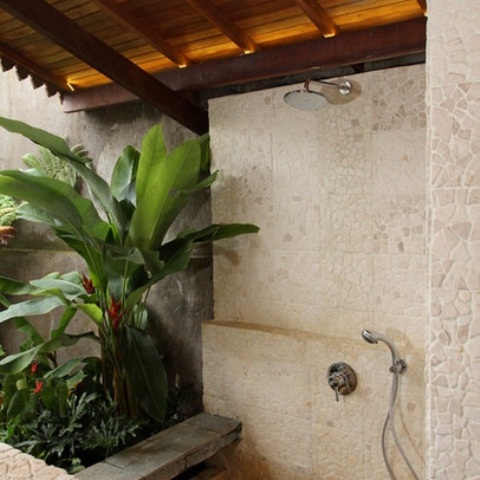 una doccia esterna rivestita con piastrelle in pietra e vegetazione tropicale piantumata