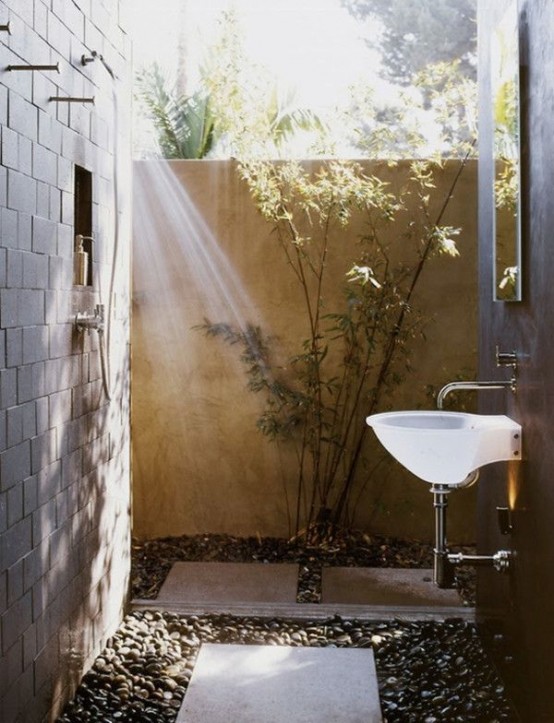 una semplice doccia esterna con ciottoli e piastrelle a terra, verde e un lavandino