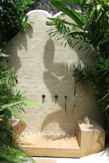 una doccia esterna con piastrelle neutre, supporto in legno e vegetazione piantumata