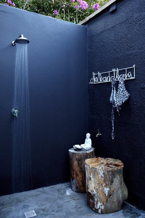 una doccia nordica da esterno realizzata con pareti nere, un pavimento in pietra e un ceppo come tavolino per gli accessori