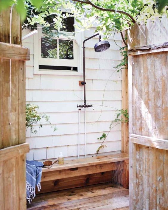 una semplice doccia esterna con panca in legno e un po 'di verde intorno