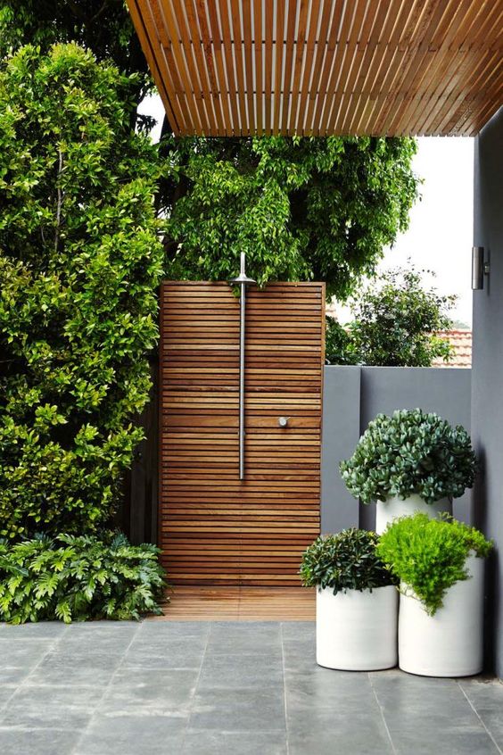 una doccia esterna minimalista con paraventi in legno, piante in vaso e doccia