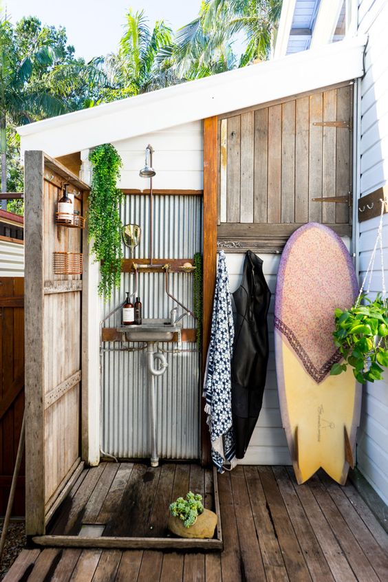 un'accogliente doccia esterna con acciaio ondulato, legno stagionato e una tavola da surf