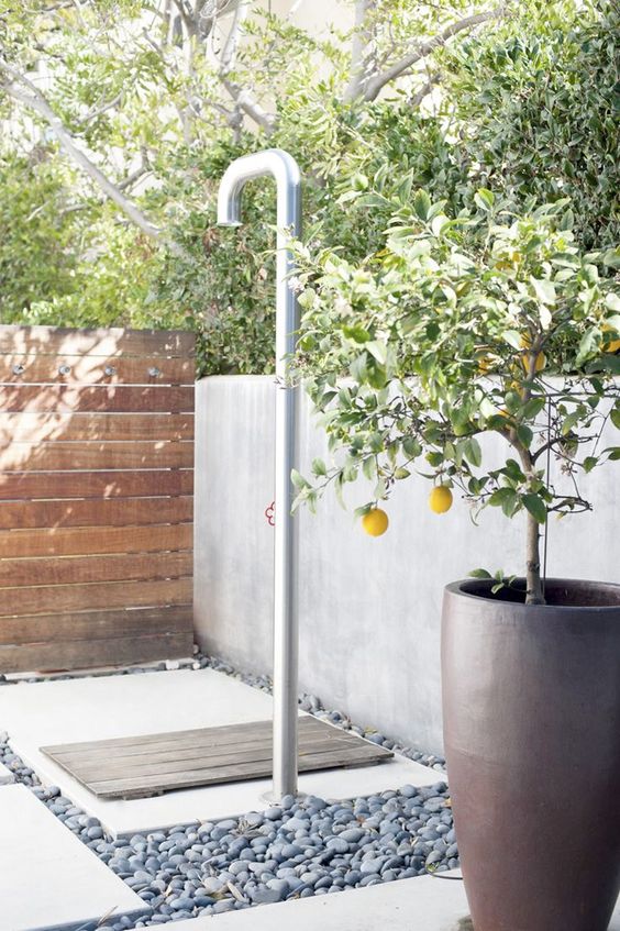 una doccia esterna contemporanea fatta con ciottoli, cemento e legno e limoni in vaso per un ambiente