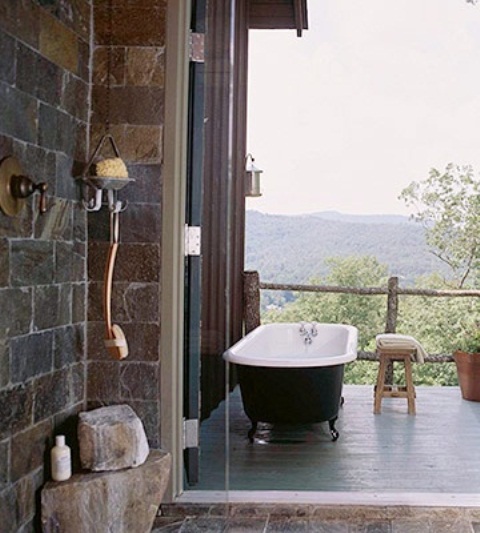 una semplice vasca da bagno all'aperto con vasca nera, tavolini in pietra e una panca in legno